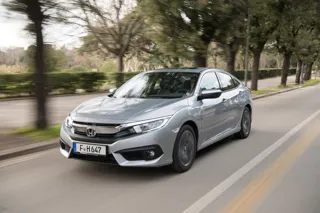Front three-quarter view of the 2018 Honda Civic saloon driving on a tree-lined street