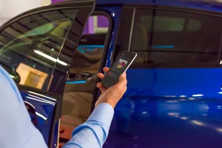 Man holds a mobile phone standing next to a blue car