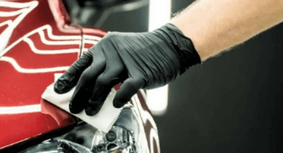 Black gloved hand polishing a red car